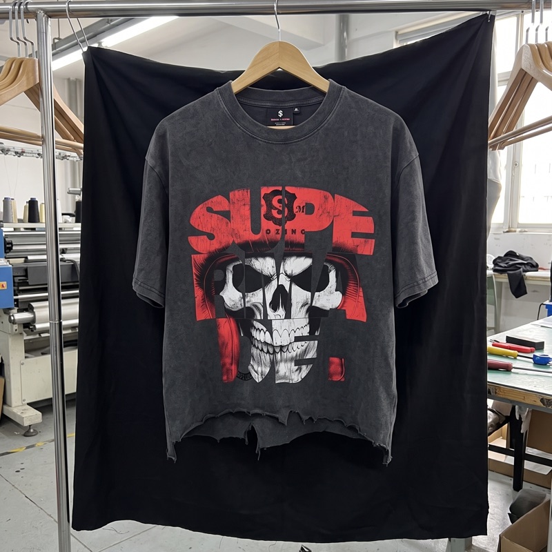 A washed black graphic tee with a red and white skull print, hanging on a rail in a factory.