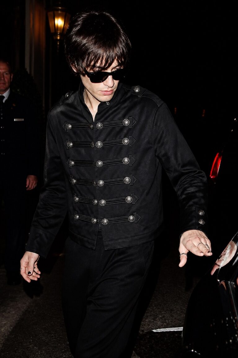 A figure in dark glasses wearing the buttoned leather jacket, photographed at night.