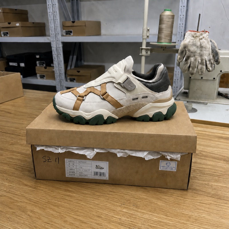 A cream and tan chunky sneaker resting on its box in a factory.