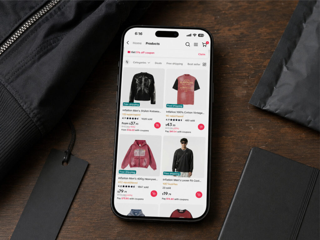 A phone on a desk showing a marketplace listing grid of jackets and tops, with folded garments alongside.