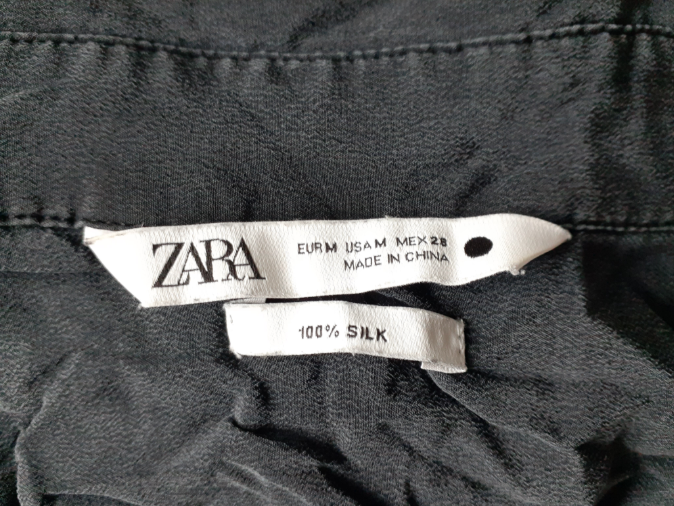 Two sewn-in labels at the neck of a black garment, the upper one carrying the brand name, size conversions and MADE IN CHINA, the lower one reading 100% SILK