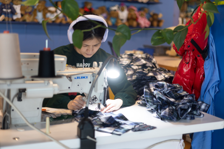 A worker operating an industrial sewing machine while joining small cut fabric components
