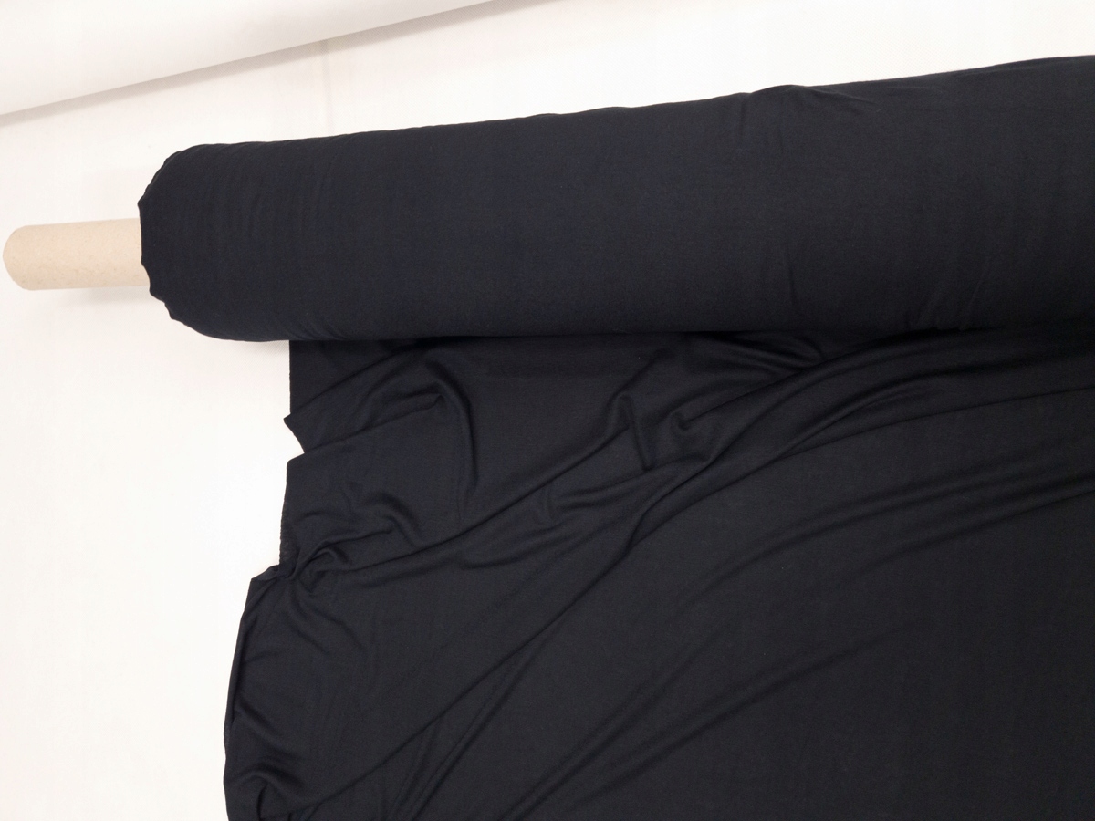 Black modal-blend knit draped from a fabric roll, showing the even dark surface that makes shade consistency and rubbing fastness important.