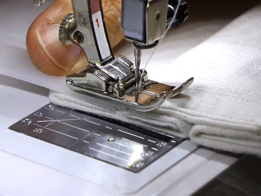 Close-up of a sewing-machine presser foot and needle stitching through several fabric layers without visible branding.