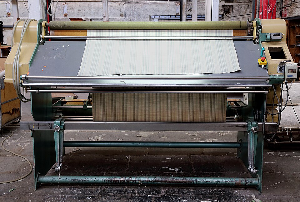 A full-width fabric inspection machine holding pale woven cloth across its viewing bed