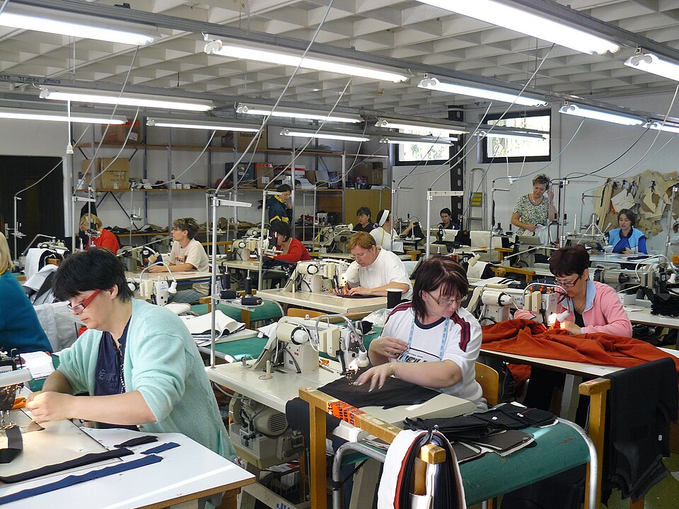 A garment sewing department with operators working at industrial sewing machines across the production floor