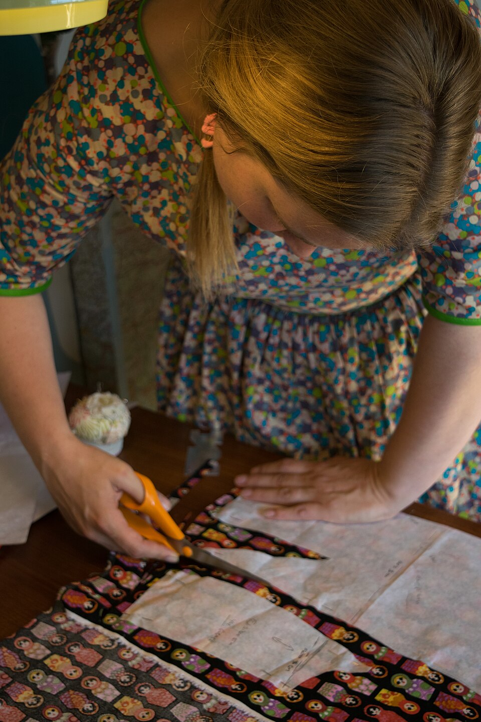 A paper garment pattern laid over printed fabric while the fabric is cut around the pattern pieces