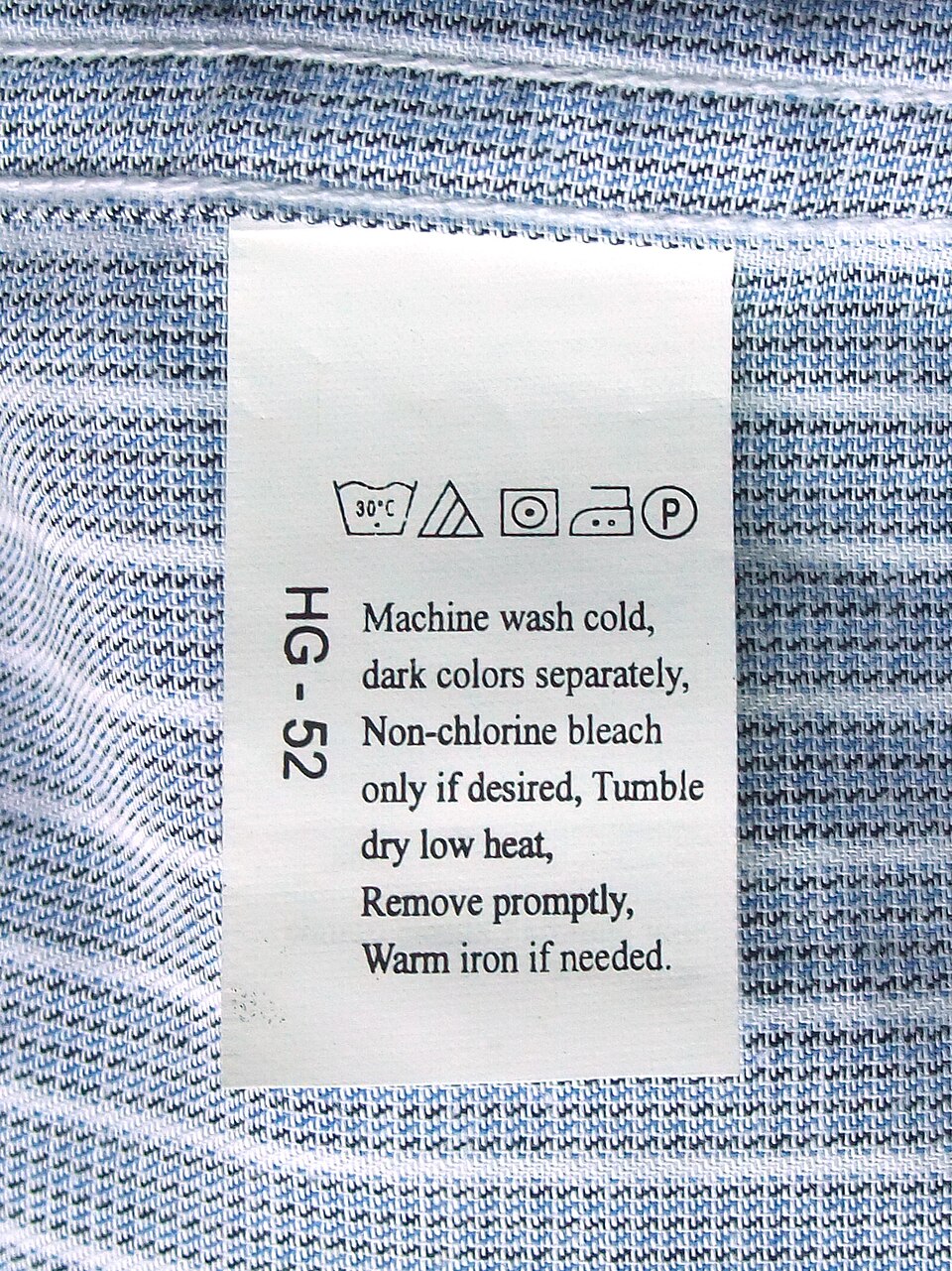 A sewn care label on denim showing laundering symbols and written washing, drying, ironing, and dry-cleaning instructions