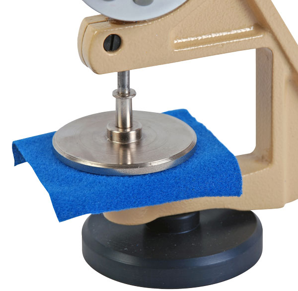 A textile thickness gauge applying a defined pressure to a fabric sample during measurement.