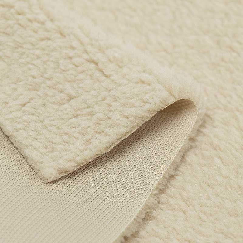 Beige sherpa fabric folded back to show the curly pile face and flatter knitted backing.