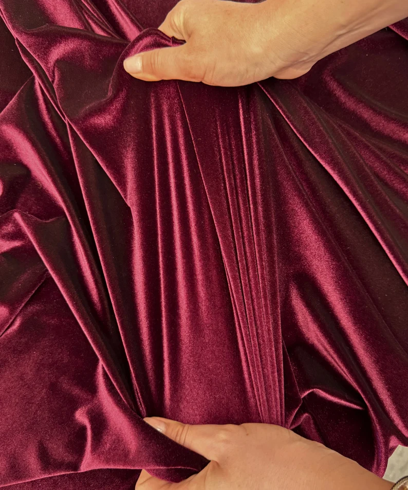 Burgundy stretch velvet pulled by hand to show extension through the fabric.