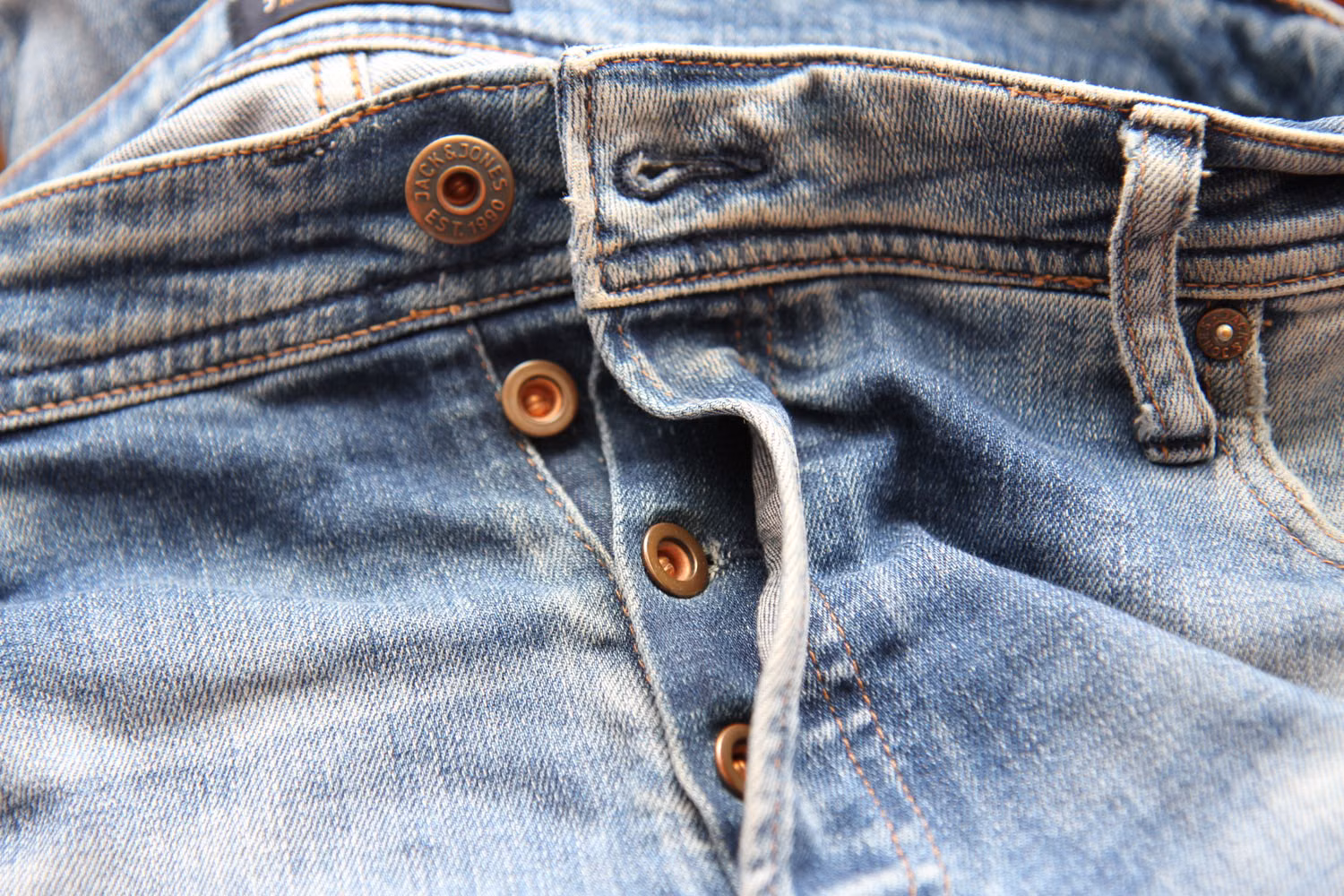 Close-up of denim jeans showing button fly, waistband, seams, stitching and metal hardware