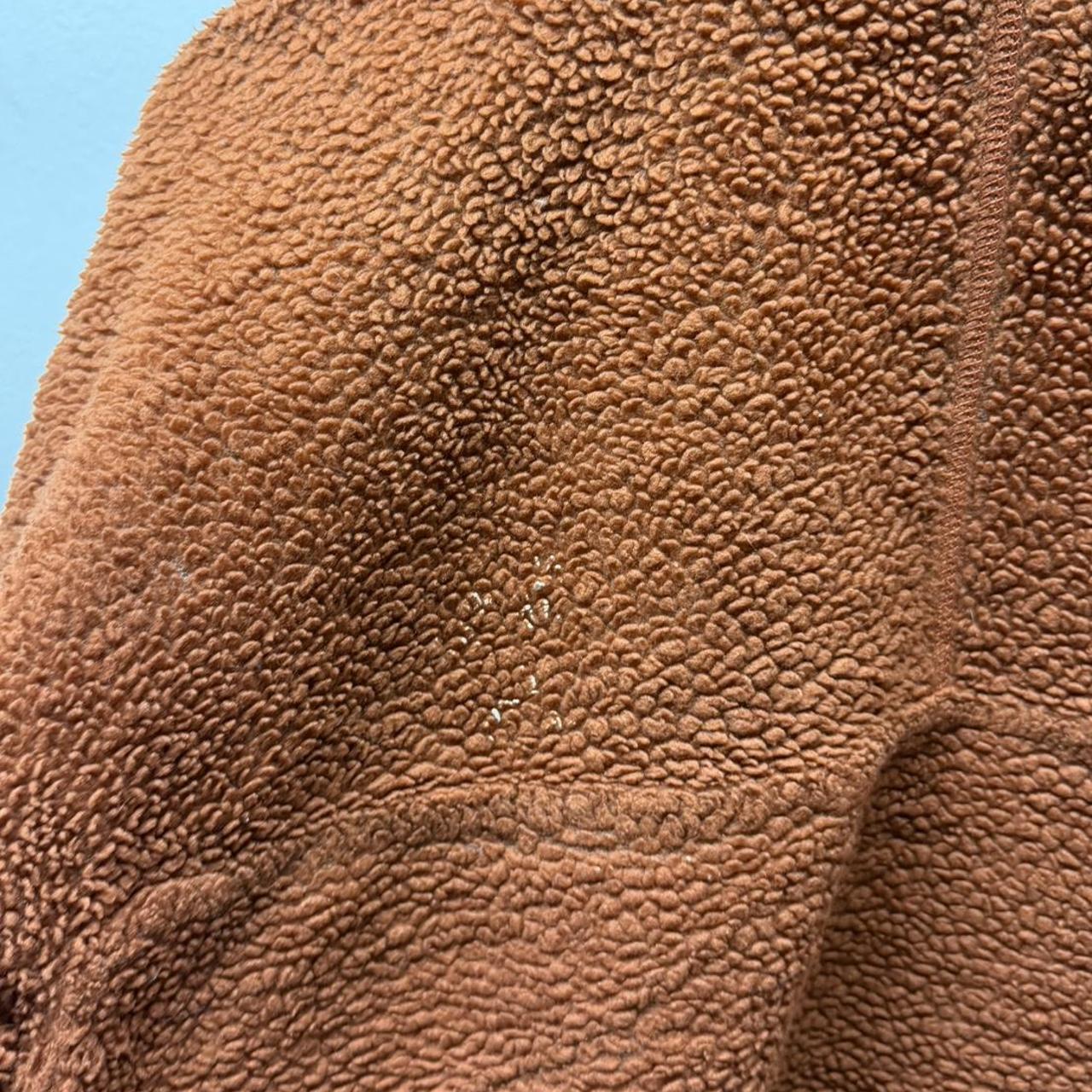 Close view of a well-worn sherpa fleece jacket showing flattened and uneven pile around a high-contact area.