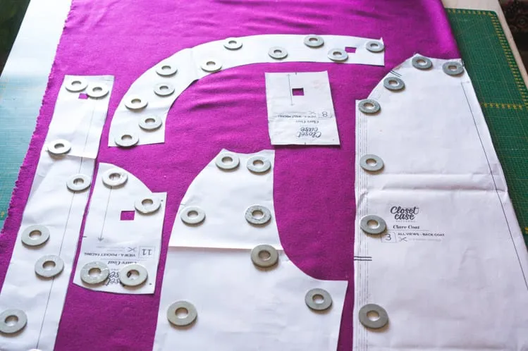 Coat cutting reference: paper pattern pieces and pattern weights arranged over magenta shell fabric