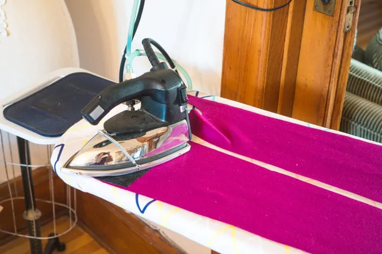 Coat pressing reference: a steam iron and layered wool coat material on a pressing surface