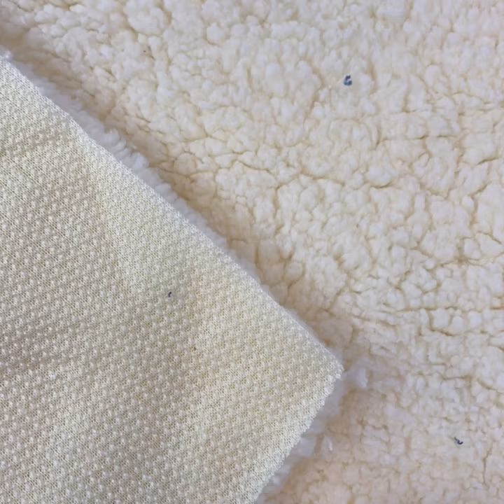 Cream sherpa compound fabric folded back to show the dense pile and a separate woven backing layer.