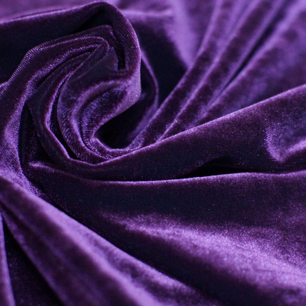 Deep purple velvet fabric arranged in folds, showing the dense pile and changing surface sheen.