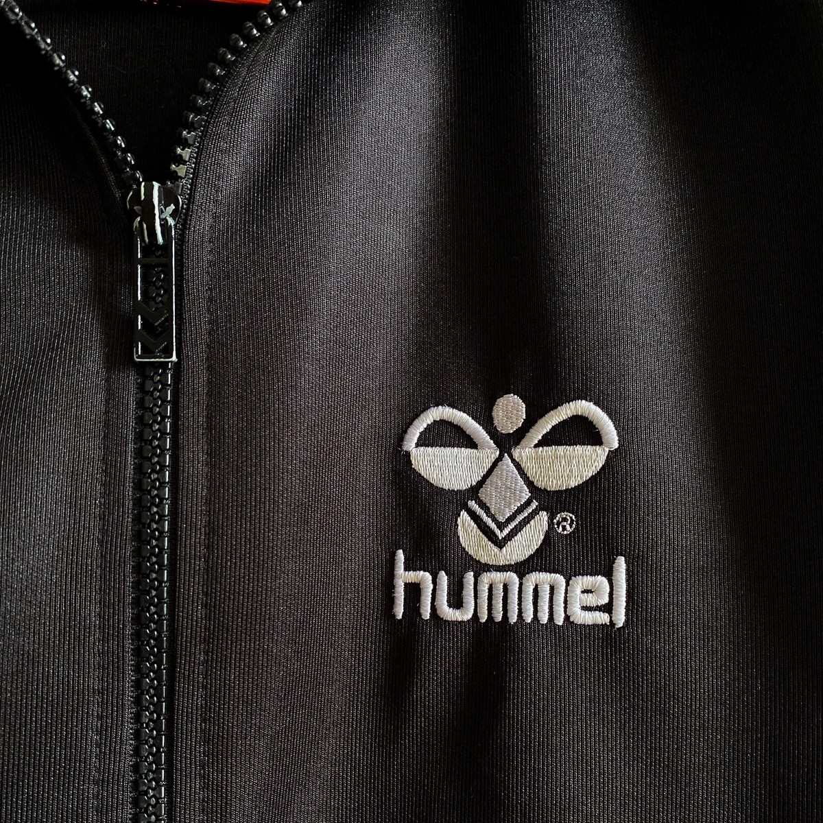 Embroidered chest logo beside a track jacket zipper