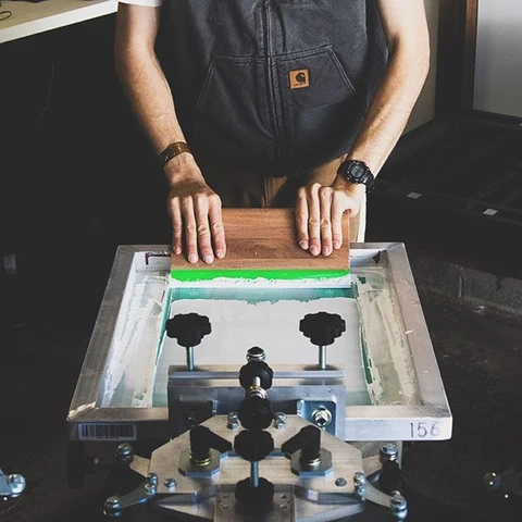 External printing reference: a screen-printing operator moving a squeegee across a screen
