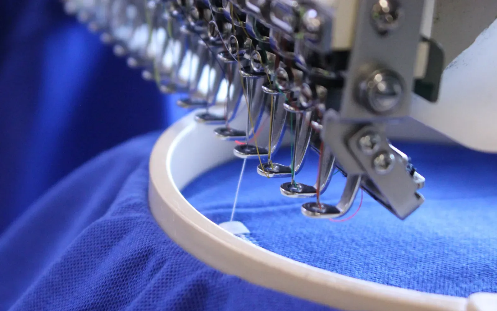 Industrial multi-needle embroidery machine stitching blue fabric.