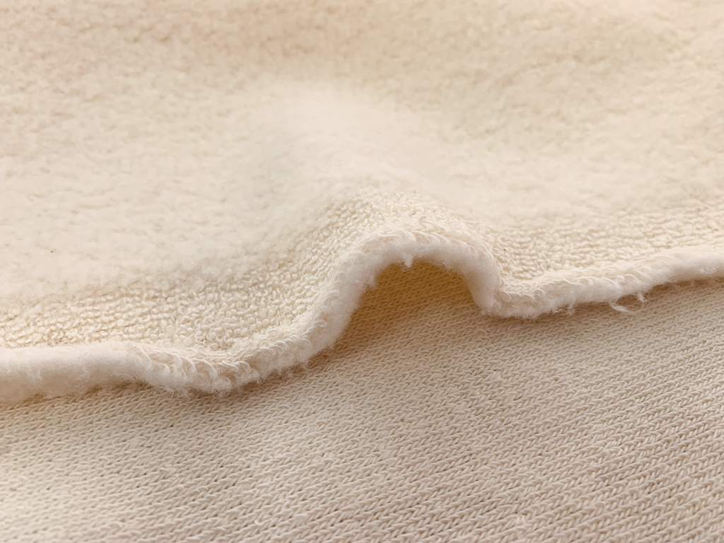 Ivory organic cotton sherpa fabric showing a thick textured surface in a natural-fiber construction.