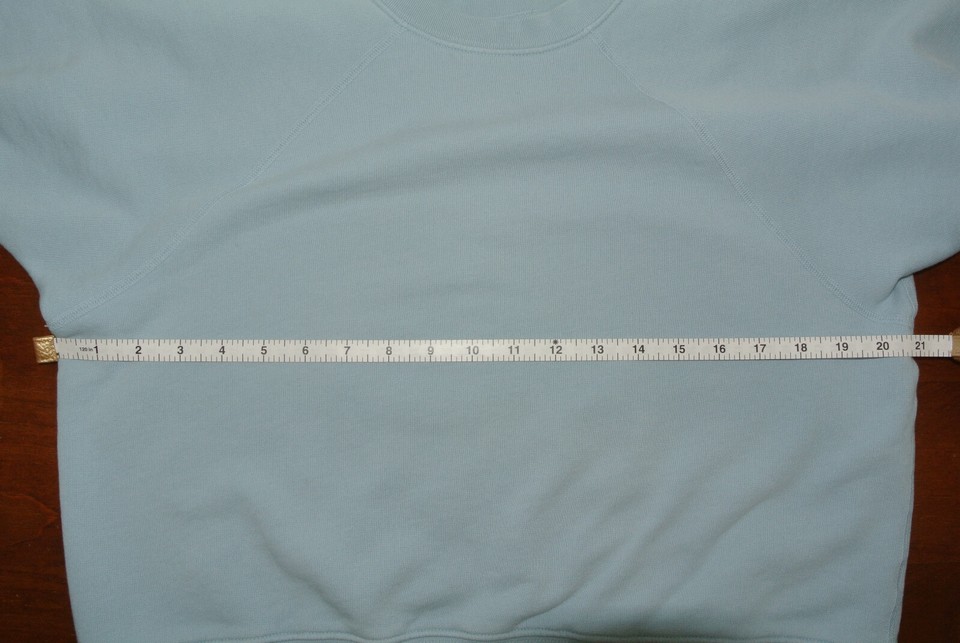 Light blue crewneck sweatshirt laid flat with a measuring tape across its chest.
