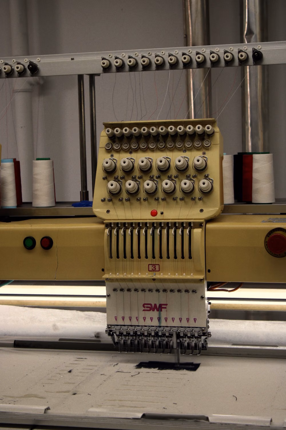 Needles and thread on an industrial embroidery machine above a fabric panel.