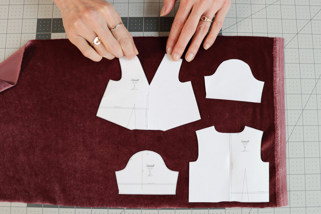 Paper garment pattern pieces laid on burgundy velvet in one consistent nap direction before cutting.