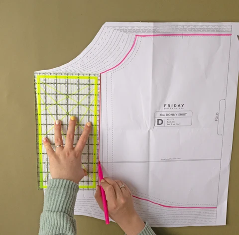 Printed multi-size paper garment pattern being checked with a ruler