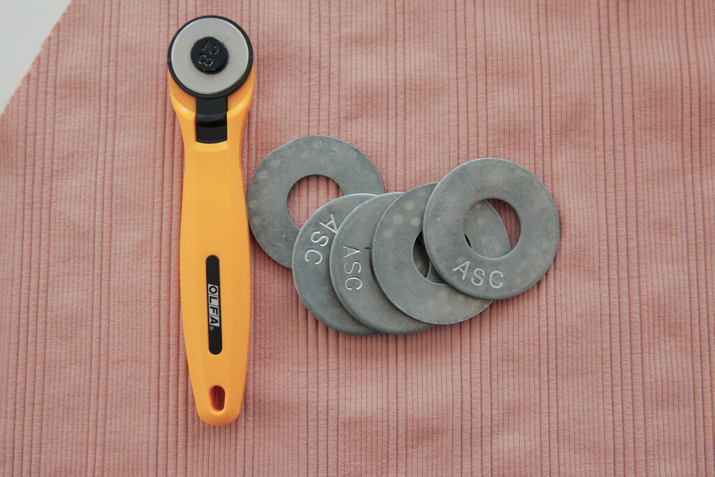Rotary cutter and round pattern weights resting on pink rib knit.