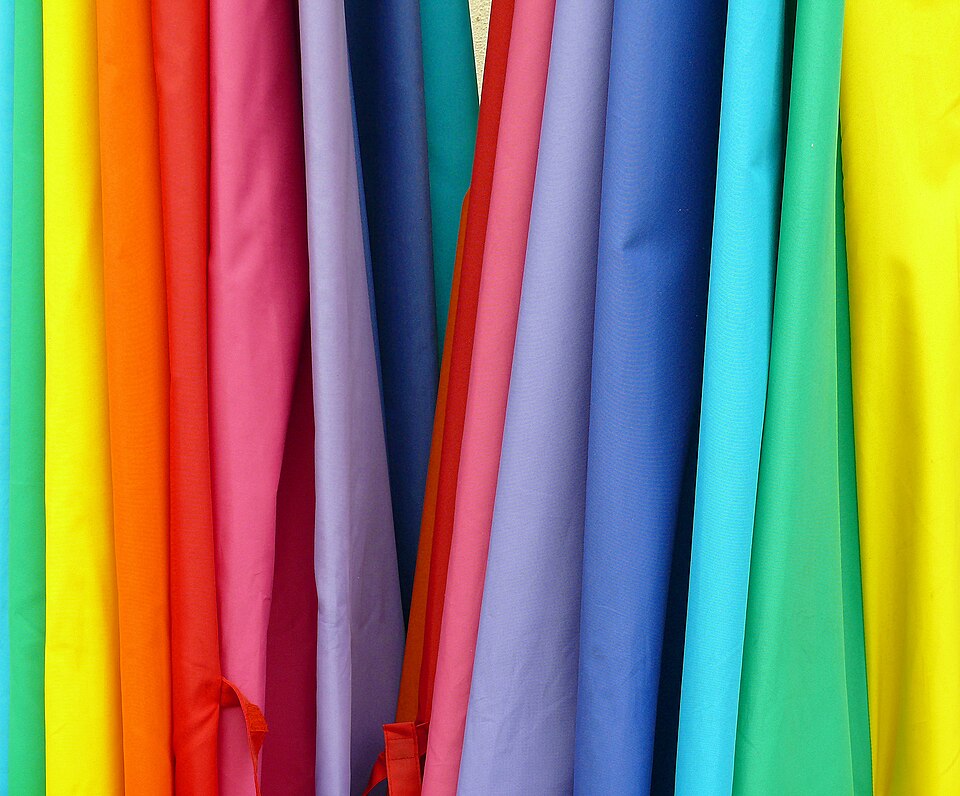 Rows of brightly colored fabric hanging side by side, illustrating the material and color choices that sit behind a garment order