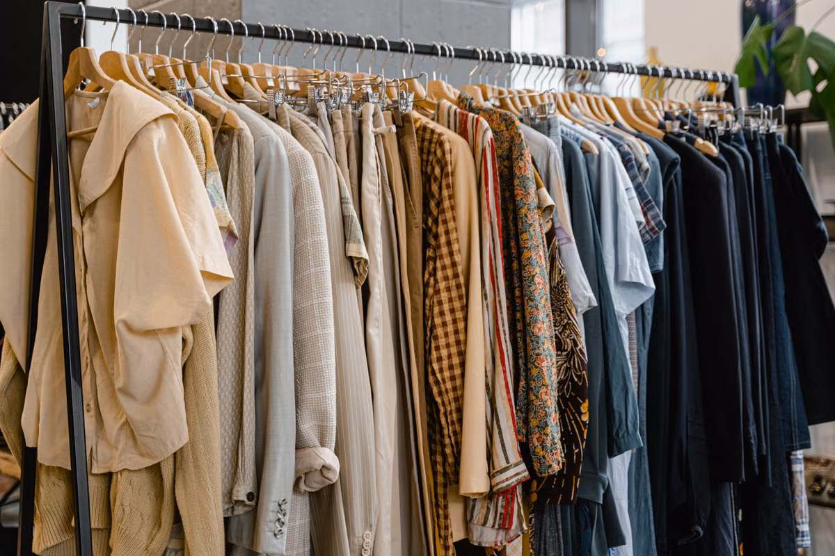 Shirts, knitwear and trousers arranged on wooden hangers along a clothing rack.